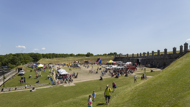 Vue entière du champ de parade du fort Numéro-Un de Lévis pendant la Fête familiale du 1er juillet avec des jeux gonflables, un camion de pompier et une foule.