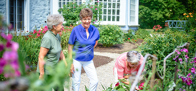 Trois dames contemplent les jardins en fleurs du lieu historique national du Manoir-Papineau en plein été.
