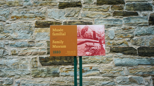 View of an interpretation panel affixed to the stone façade of the family museum located at the Manoir Papineau National Historic Site