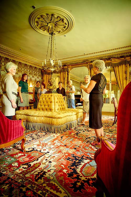 Des dames visitent le salon jaune du lieu historique national du Manoir-Papineau avec une employée de Parcs Canada.