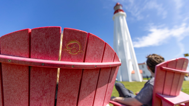 A visitor admires the Pointe-au-Père Lighthouse from a red chair. 