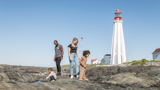 A family explores the coastline near a lighthouse.