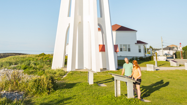Two visitors read an interpretation panel near a lighthouse. 