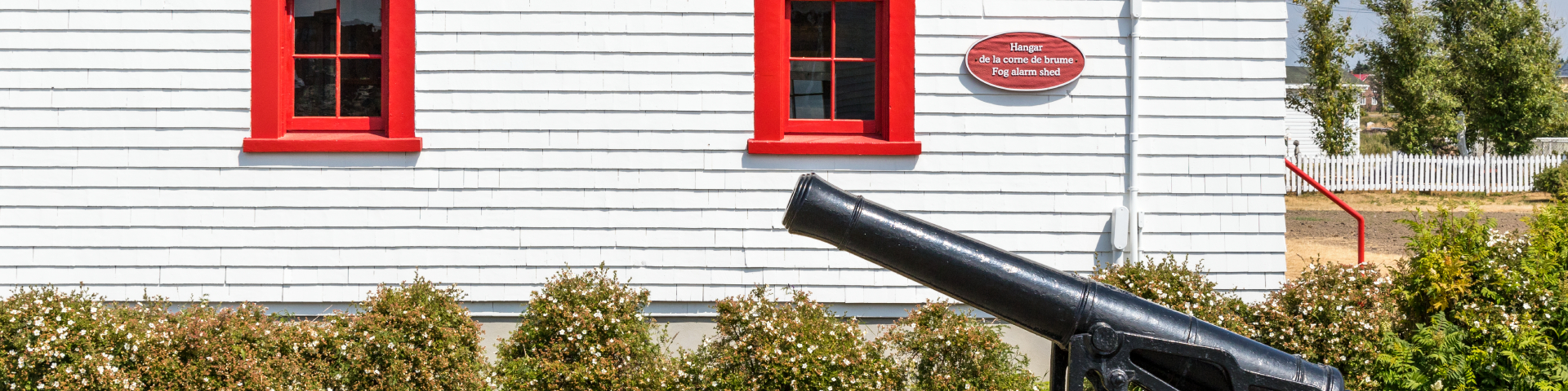 Exterior wall of a plank-wooded heritage building with a cannon at the bottom. 