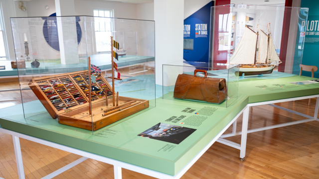 Coffret de bois, mallette et voilier miniature sur une table dans un musée. 