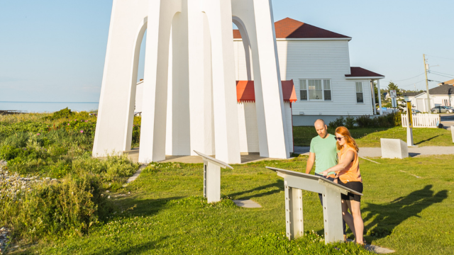 Two visitors read an interpretation panel at the foot of a lighthouse.