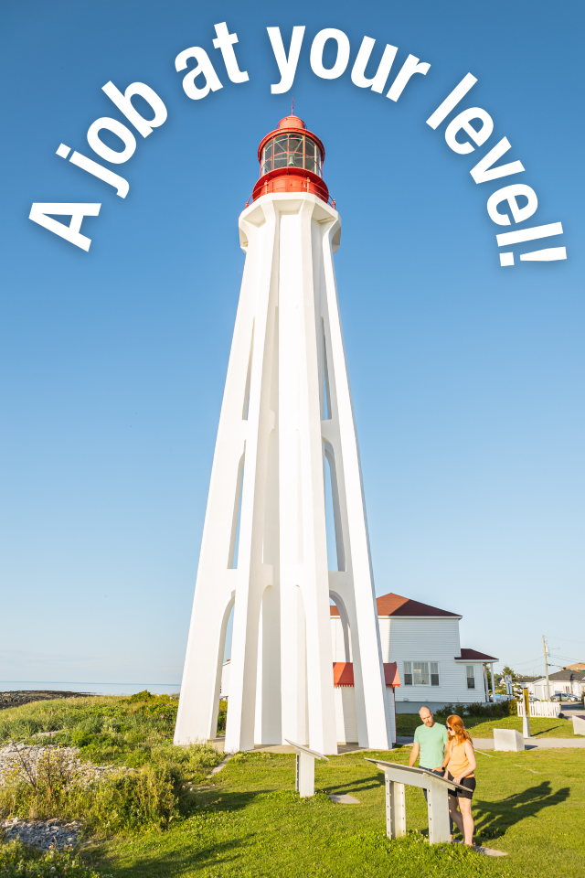 Two visitors read an interpretation panel at the foot of a white lighthouse. 