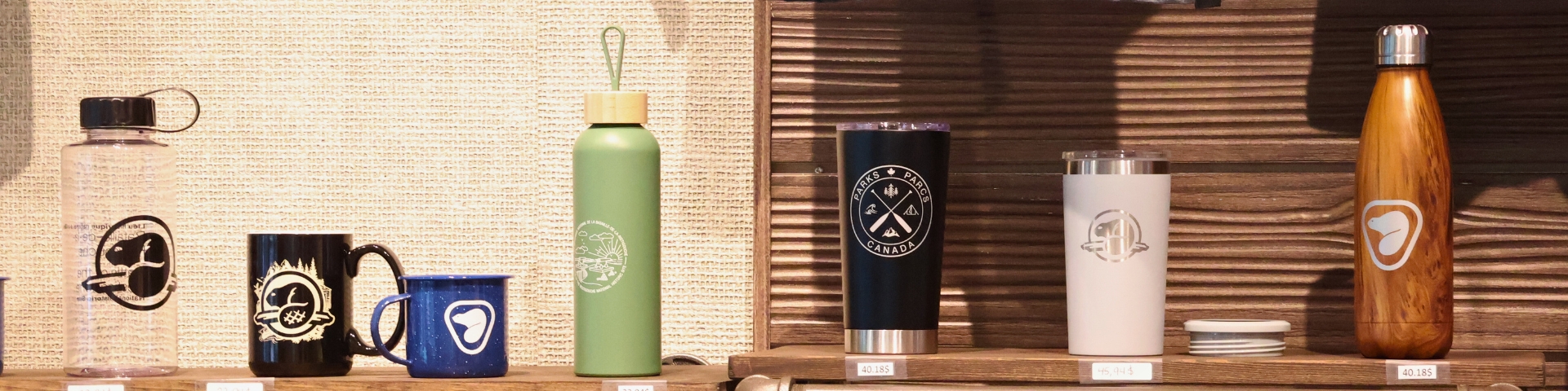 Articles de Parcs Canada comme des bouteilles, tasses et gobelet sur une étagère de bois.