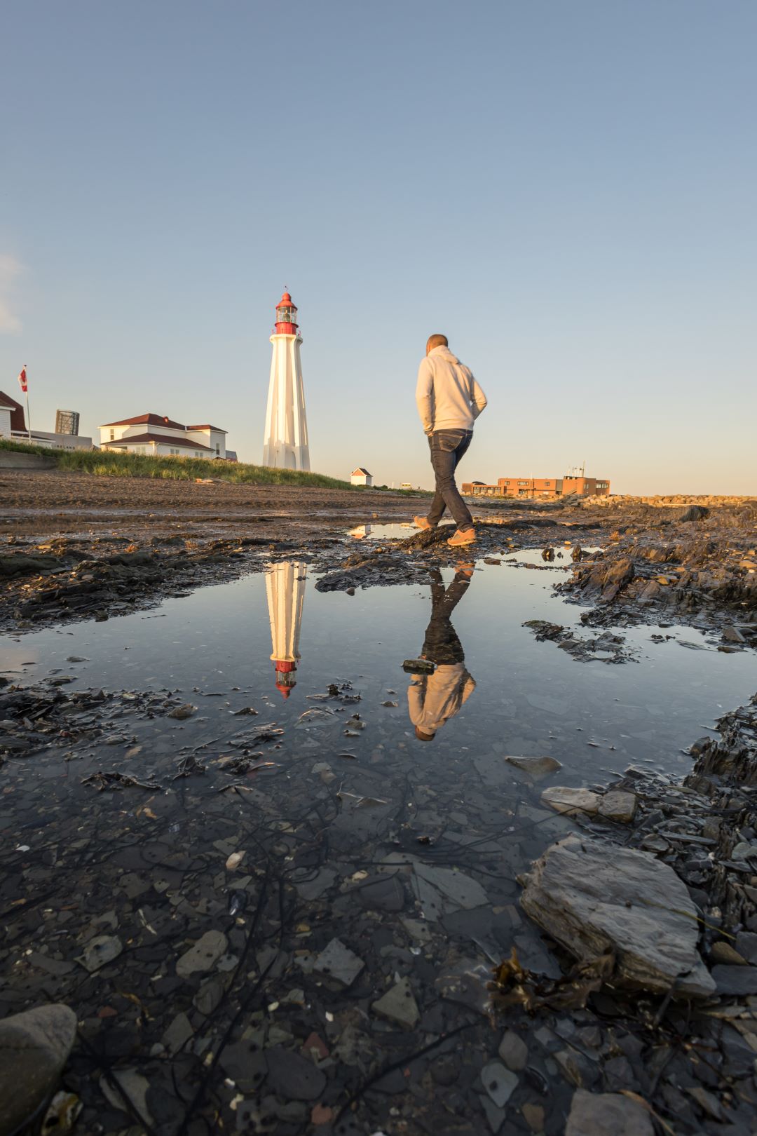 A man walks on the shore with the lighthouse in the back.