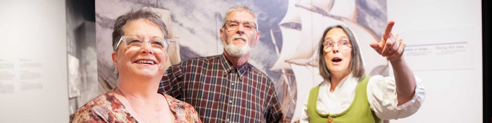 Three visitors in their 60s are reacting to an exhibit. 