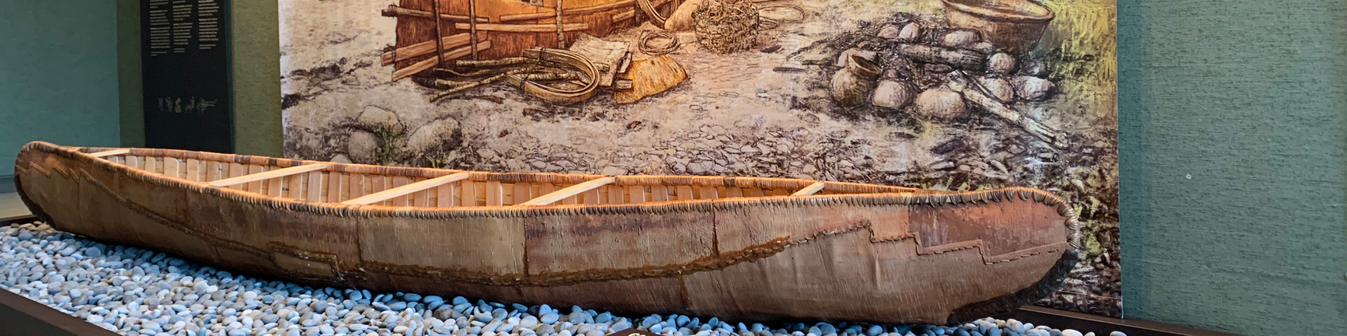 Un canot d'écorce est posé sur un lit de pierres de rivière dans une exposition.