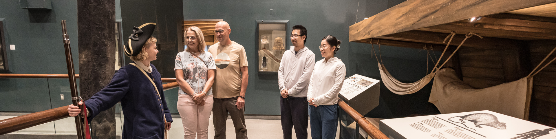 A group of visitors listens to an interpreter dressed as a French soldier in an exhibit. 