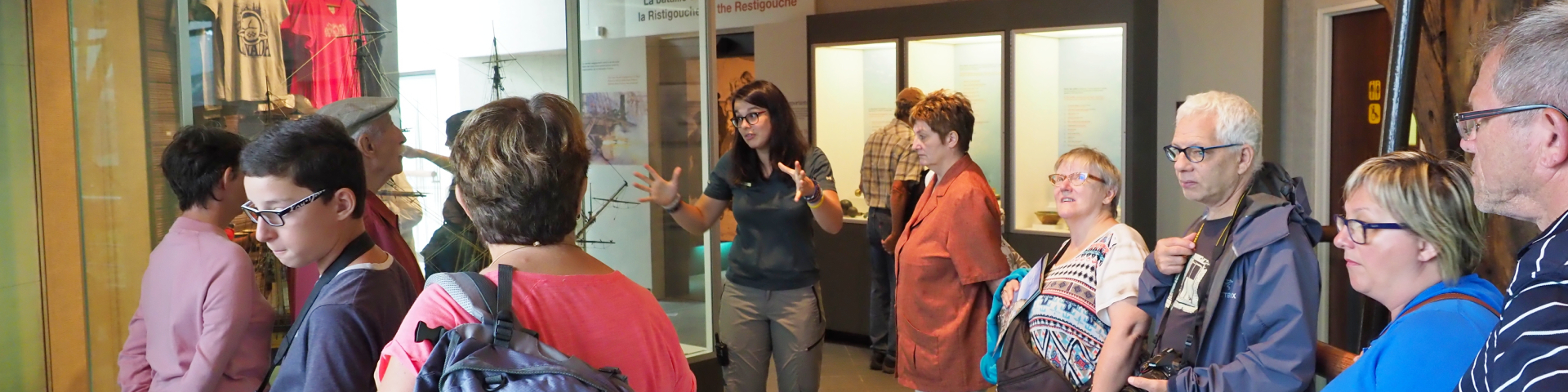 Un groupe de voyageurs dans un musée écoutent une guide interprète. 