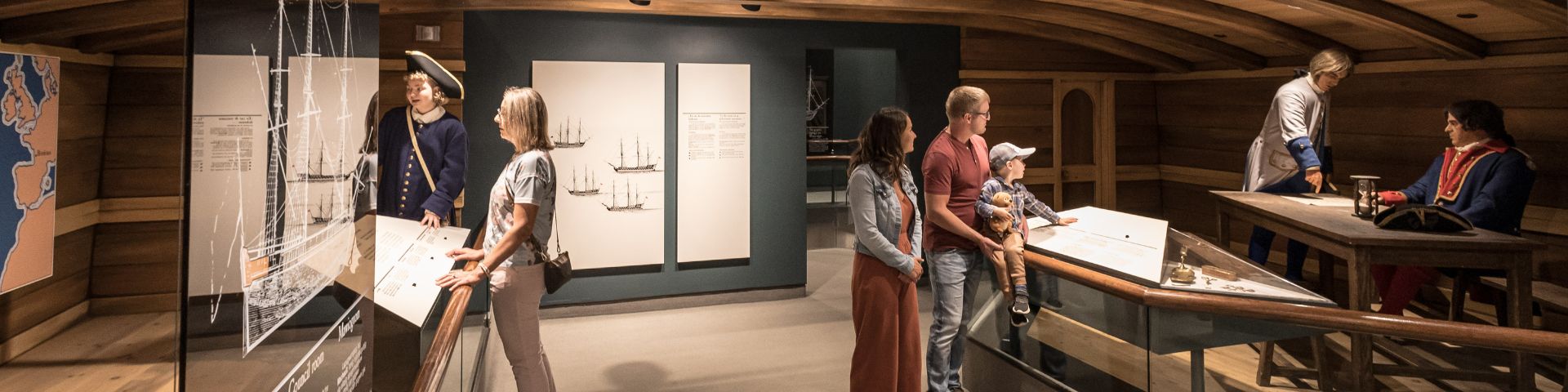 Visitors accompanied by an interpreter dressed as a soldier explore an exhibition room representing the command centre of a ship.  