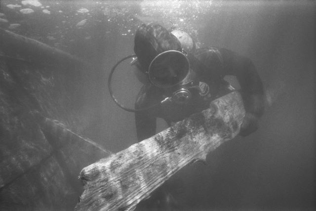 Black and white photo of a scuba diver holding a piece of wreckage.