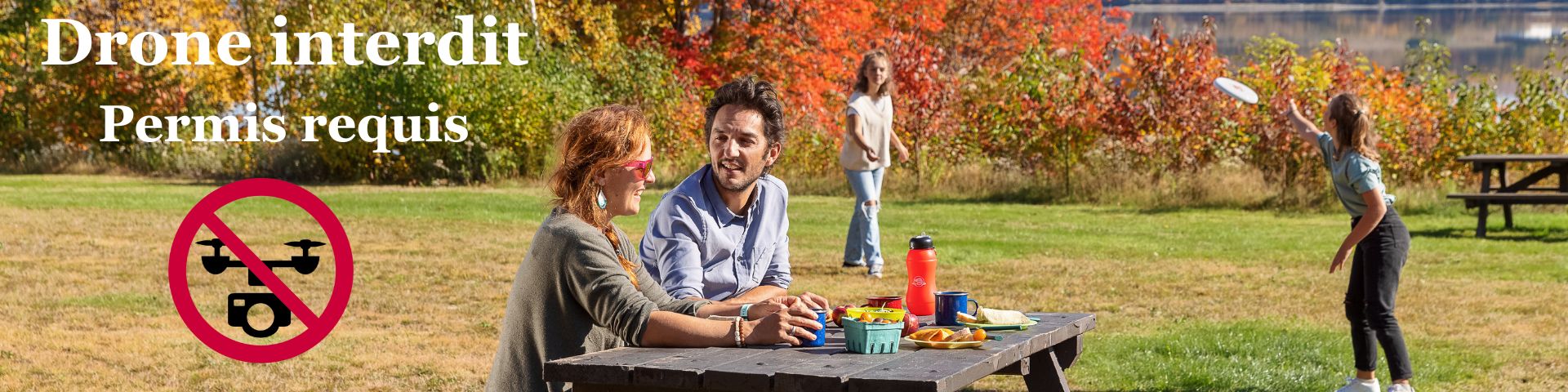Un couple discute à une table de piquenique pendant que des enfants jouent derrière sur un terrain gazonné. 
