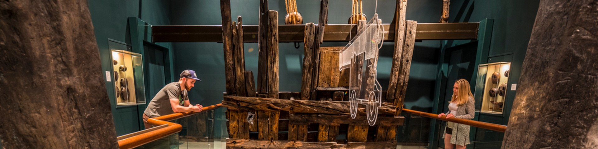 Two visitors admire the remains of the vessel Le Machault in a museum.