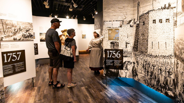 Une employée en costume d'époque fait faire une visite guidée dans un musée à deux personnes. 