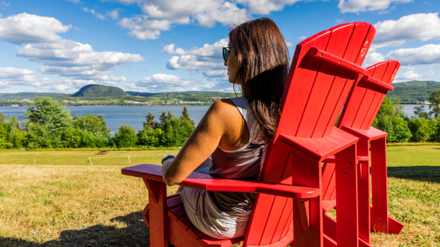 A woman sitting in a red chair admires the river. 