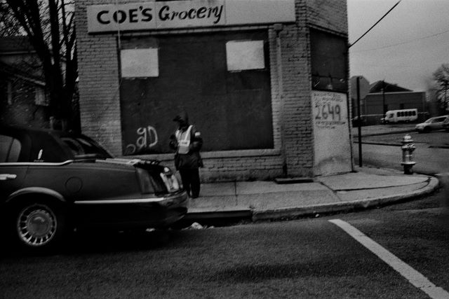 A man stands on a sidewalk in front of a boutique next to a car.