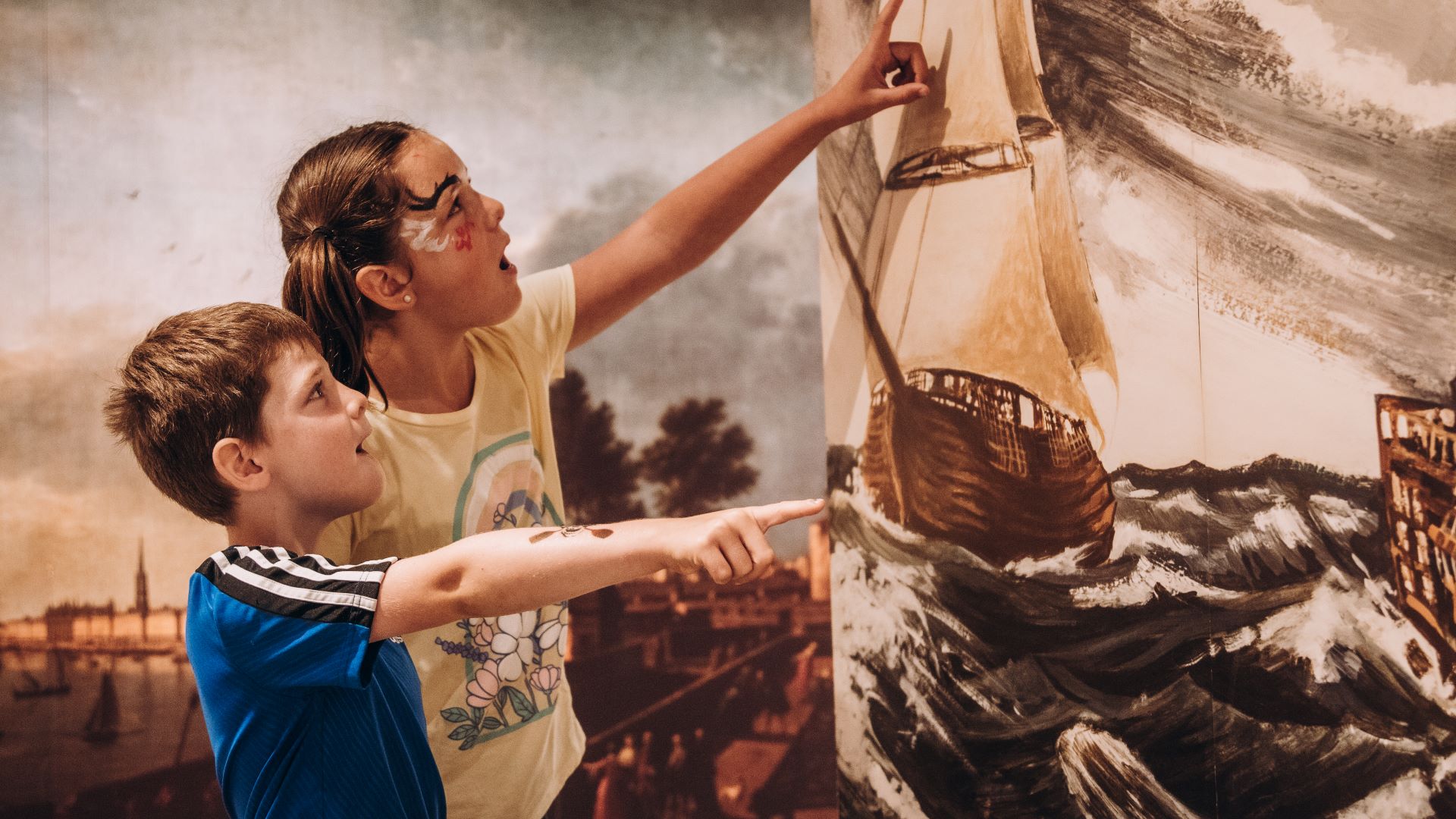 Two children point to a canvas showing a 17th-century warship. 