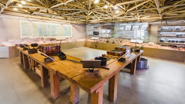 Wooden tables displaying artifacts and cast-iron objects in the Blast Furnace building at Forges du Saint-Maurice National Historic Site.