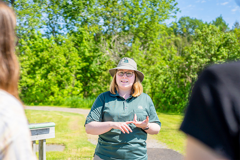 Photo of a Forges du Saint-Maurice National Historic Site guide providing a tour to visitors. They are outside the Grande Maison.