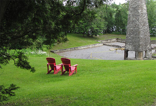 Deux chaises rouges de Parcs Canada dans la verdure devant la forge basse