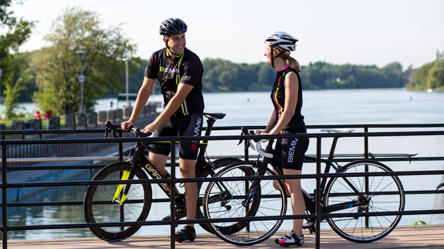 Two smiling cyclists walking their bikes over a footbridge at the Canal-de-Saint-Ours.