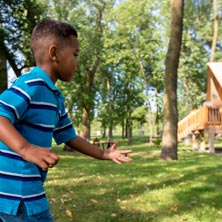 Un enfant joue en plein air sur un site de camping boisé, lançant un jeu coloré près de tentes sur pilotis, dans une ambiance naturelle et familiale.