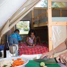 Une mère qui cuisine dans une tente oTENTik pendant que les enfants s'amusent derrière.