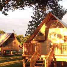 Tentes prêtes à camper au coucher du soleil, installées dans un terrain verdoyant avec arbres et table de pique-nique, offrant un hébergement nature confortable.