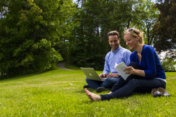 Un homme et une femme heureux qui utilisent un ordinateur portable, assis sur la pelouse
