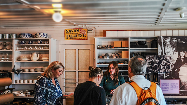 A female Parks Canada guide is explaining historical facts to a group of adult visitors during a tour of the Louis S. St. Laurent National Historic Site.