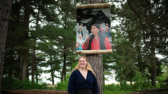 An Algonquin artist, Nika Paul, stands proudly in front of one of her four paintings on display at Obadjiwan–Fort Témiscamingue National Historic Site; this piece depicts an Indigenous adult woman.