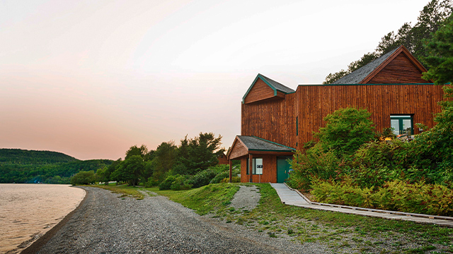 A view of a pink-orange sky at sunset over Lake Témiscamingue, with the visitor and interpretation centre of Obadjiwan–Fort Témiscamingue National Historic Site at the end of a summer day.