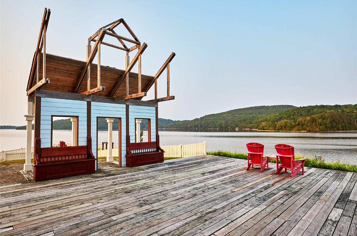 Obadjiwan–Fort Témiscamingue National Historic Site's chapel with two red chairs on a patio, facing a bay.