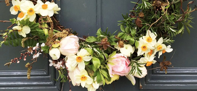 Couronne décorative apposée sur une porte et fabriquée à l’aide de branches de sapin, de fleurs sauvages et de branches de bois par l’artisane Malie Lessard-Therrien.

