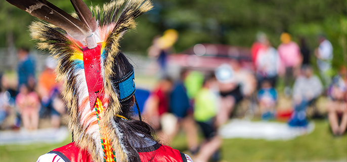 Un danseur traditionnel Algonquin vêtu d’une régalia et d’une coiffe ornée de plumes fait face à la foule durant un pow-wow au lieu historique national d’Obadjiwan-Fort-Témiscamingue.