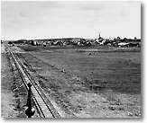 Black and white picture of a railway, a field, and a distant village.
