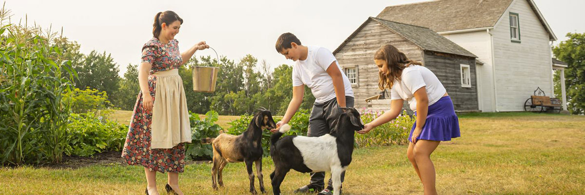 Two children help a Parks Canada interpreter feed goats by the garden