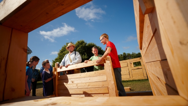 Un interprète et des visiteurs discutent au pied d'une structure de bois.