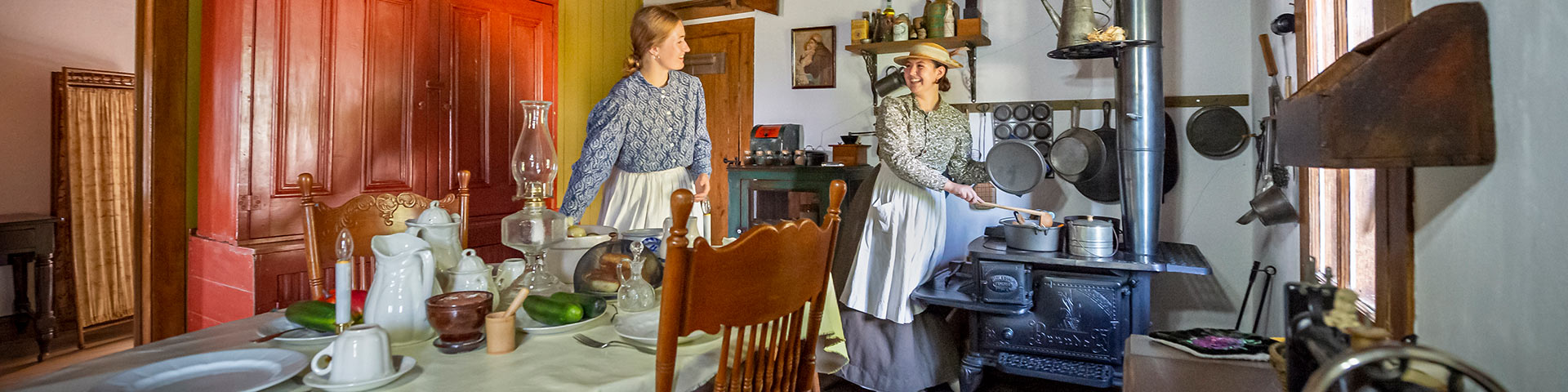 Two Parks Canada interpreters in historical costume setting the table in the Rectory. 