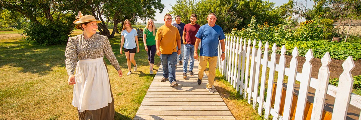 A Parks Canada interpreter in historical costume walking alongside a group of visitors on a boardwalk.