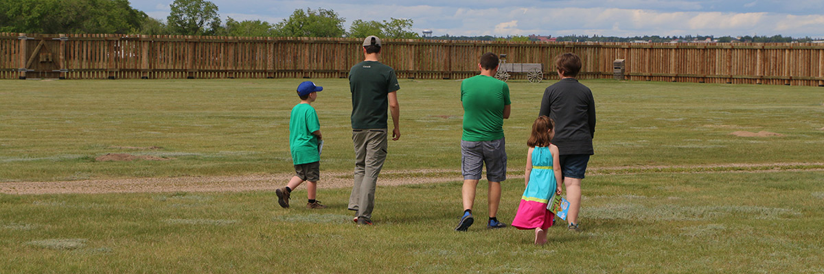 Parks Canada staff person and visitors walk across the grounds at Fort Battleford National Historic Site. 