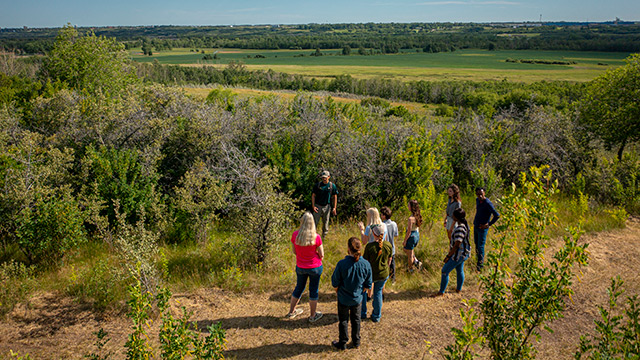 A Park Canada interpreter with a group of visitors along the trail with views towards the river. 