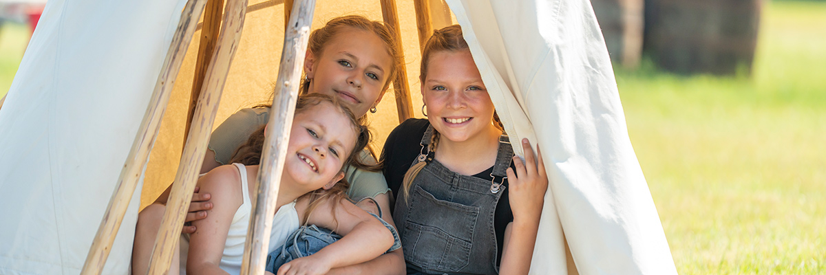 Three children sit inside a mini tipi.