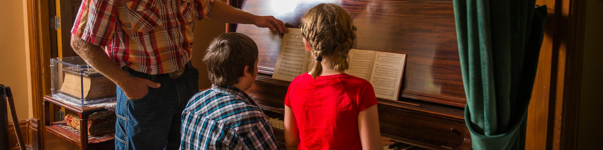 Famille réunie autour d'un piano pour en apprendre plus sur la musique jouée dans la maison de pierres au lieu historique national du Homestead-Motherwell