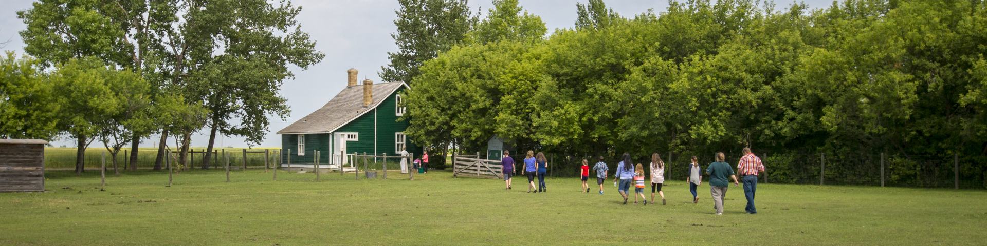 A group of people walking to the hired man's cottage through the barnyard, for an interpretive program at Motherwell Homestead National Historic Site.