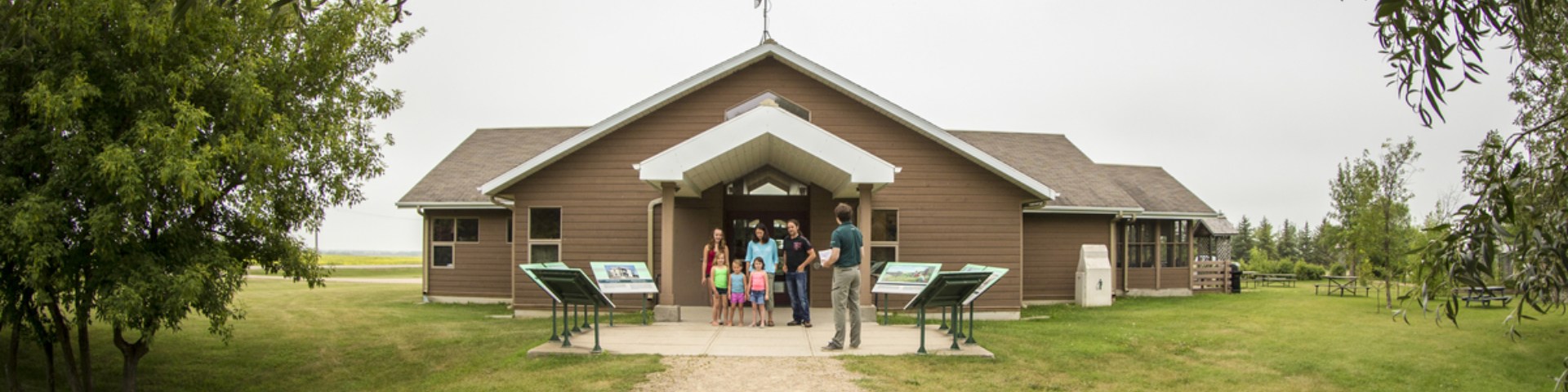  Un interprète en uniforme explique le plan du site à un groupe d'adultes et de jeunes enfants à l'extérieur du centre d'accueil du lieu historique national du Homestead-Motherwell.